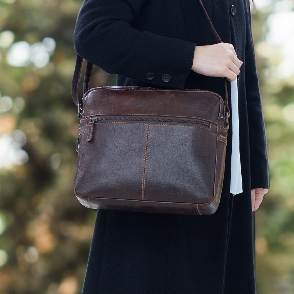 Person holding a brown leather bag with a blurred natural background