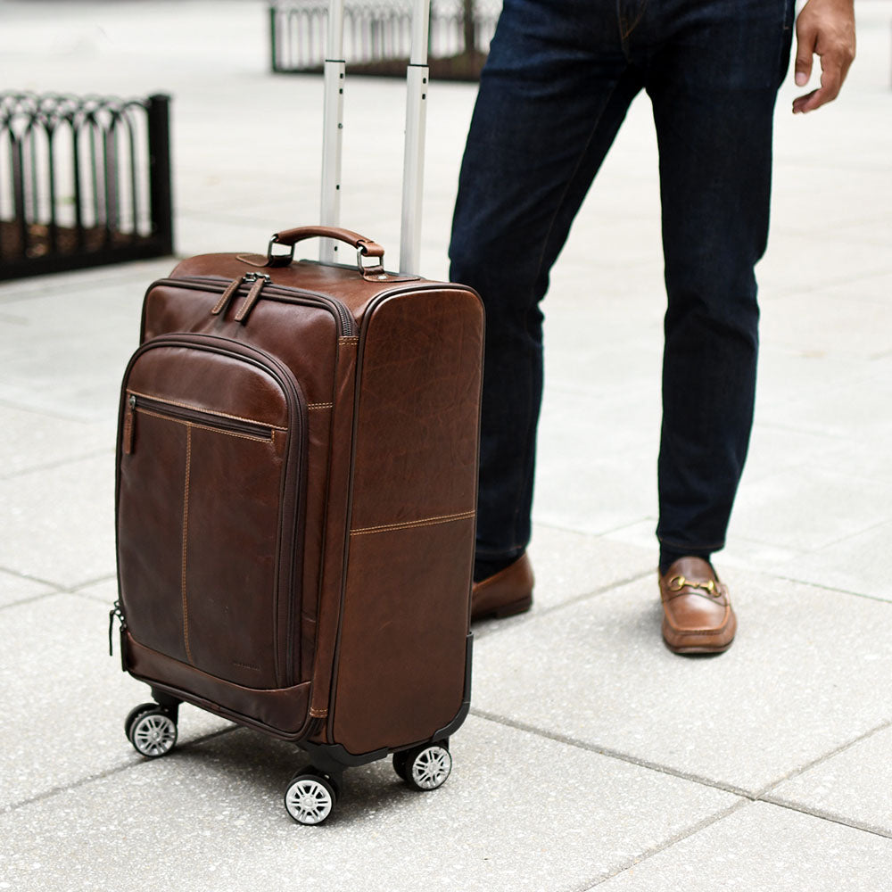 Brown suitcase with wheels on a tiled floor, person partially visible
