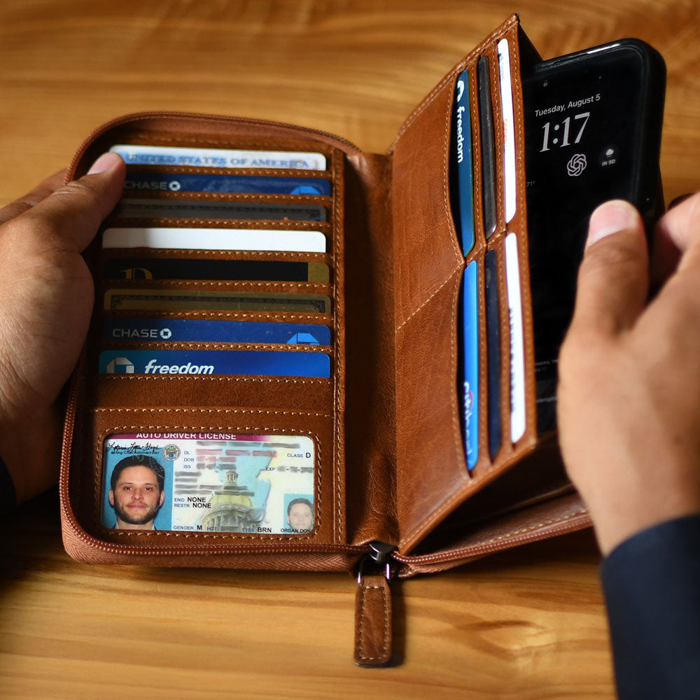 Brown leather wallet with cards and a phone, held by hands on a wooden surface