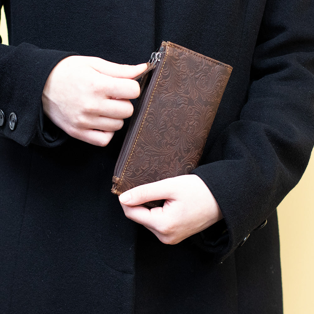 Person holding a brown leather wallet with intricate patterns against a dark background